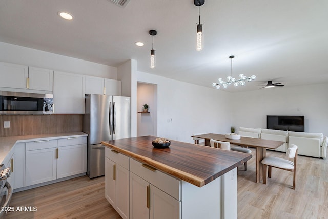 kitchen with butcher block counters, light wood-style flooring, appliances with stainless steel finishes, a center island, and pendant lighting