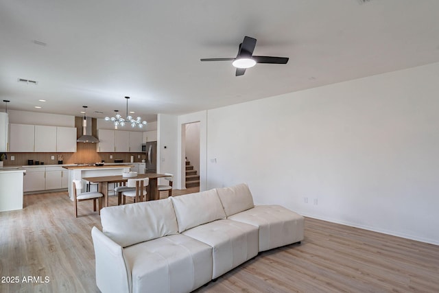 living area with light wood finished floors, stairs, visible vents, and ceiling fan with notable chandelier