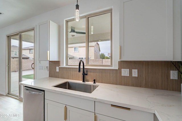 kitchen featuring light stone counters, white cabinets, a sink, and dishwasher