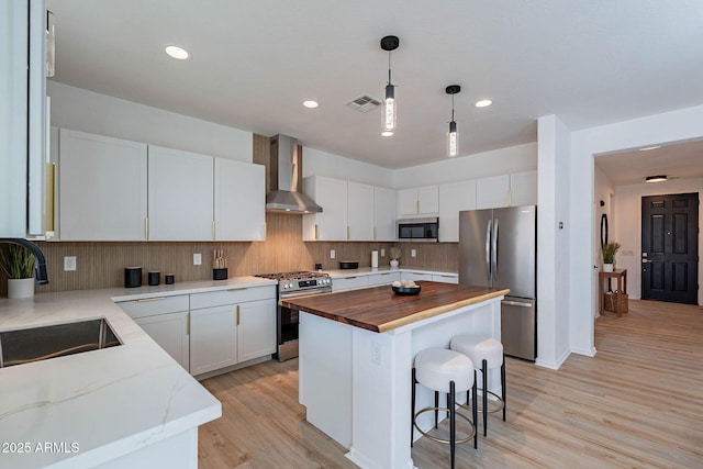 kitchen with visible vents, wall chimney exhaust hood, butcher block counters, stainless steel appliances, and a sink