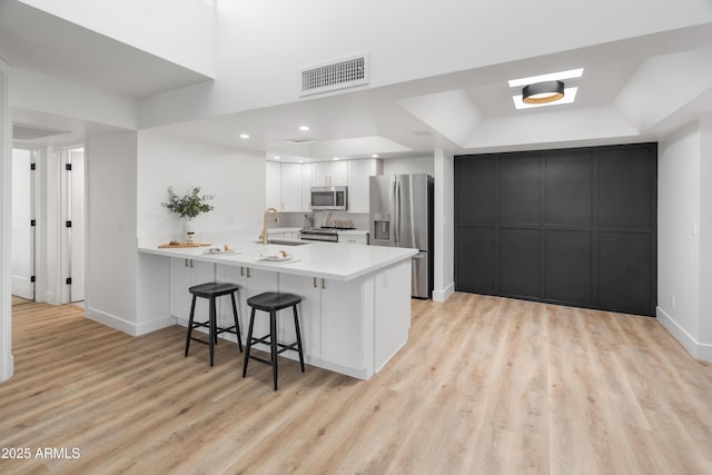 2935 N 68th St Unit 205, Scottsdale, AZ 85251 - kitchen featuring stainless steel appliances, a peninsula, a breakfast bar, a raised ceiling, and light wood-style floors