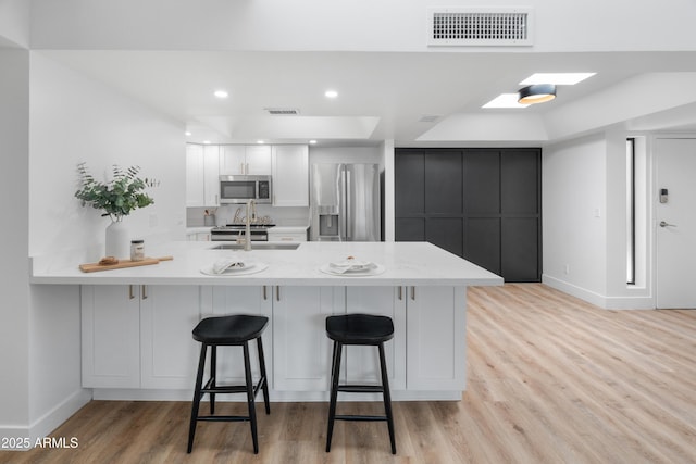 2935 N 68th St Unit 205, Scottsdale, AZ 85251 - kitchen with appliances with stainless steel finishes, light wood-style flooring, a kitchen breakfast bar, a peninsula, and white cabinetry