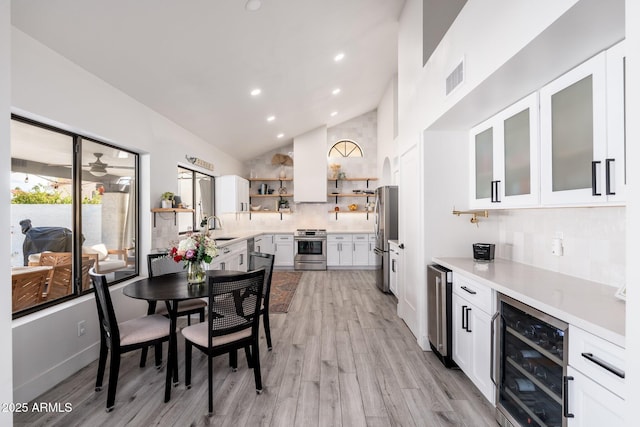 dining room featuring light hardwood / wood-style floors, high vaulted ceiling, sink, and beverage cooler