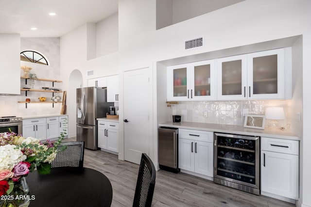 kitchen with white cabinetry, light hardwood / wood-style floors, backsplash, appliances with stainless steel finishes, and beverage cooler