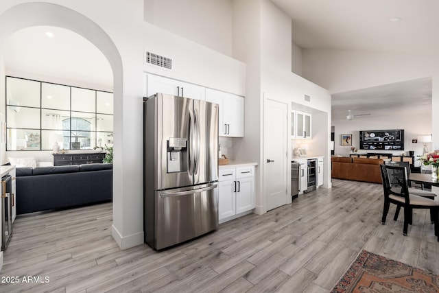 kitchen featuring stainless steel fridge with ice dispenser, light hardwood / wood-style flooring, wine cooler, high vaulted ceiling, and white cabinets