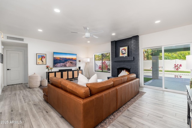 living room with ceiling fan, light hardwood / wood-style floors, and a brick fireplace