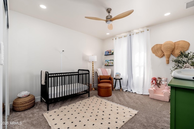 carpeted bedroom with ceiling fan and a crib