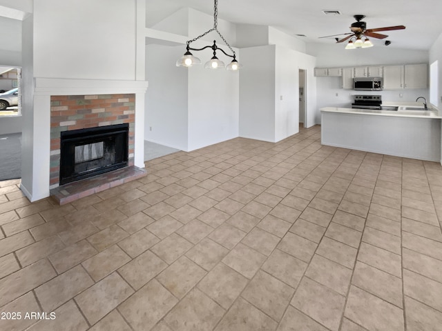 unfurnished living room featuring a fireplace, lofted ceiling, sink, light tile patterned floors, and ceiling fan