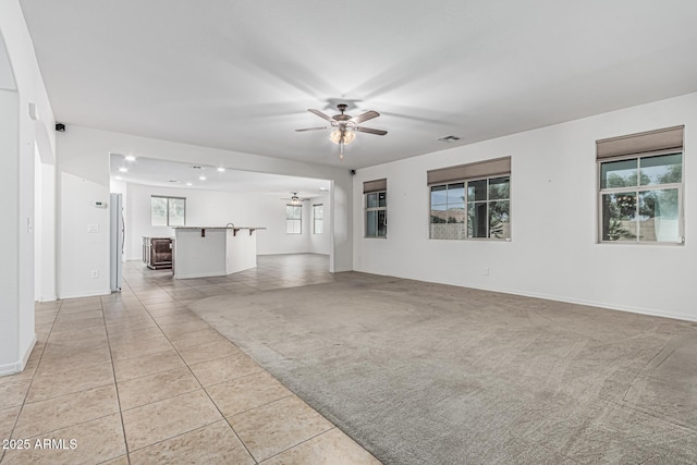 unfurnished living room featuring light carpet, baseboards, visible vents, ceiling fan, and light tile patterned floors