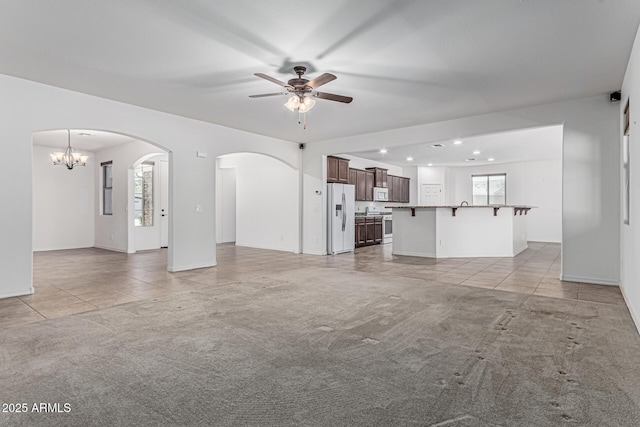 unfurnished living room with light carpet, arched walkways, baseboards, ceiling fan with notable chandelier, and light tile patterned floors