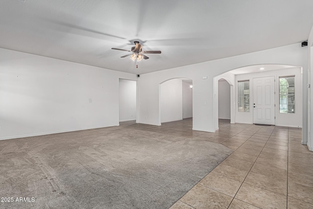unfurnished living room with tile patterned floors, a ceiling fan, and arched walkways