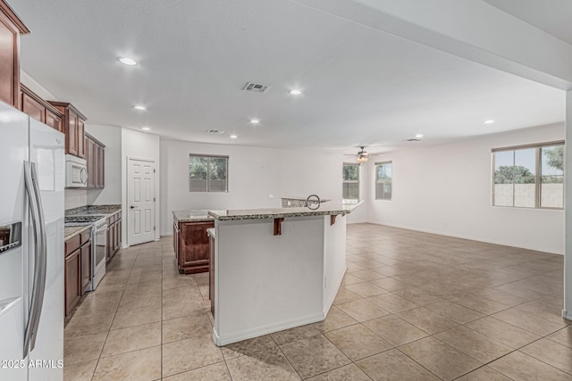 kitchen with a ceiling fan, fridge with ice dispenser, white microwave, gas stove, and a kitchen island