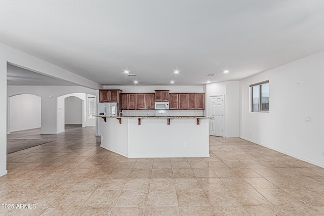kitchen featuring a kitchen breakfast bar, a large island, arched walkways, white microwave, and stainless steel fridge
