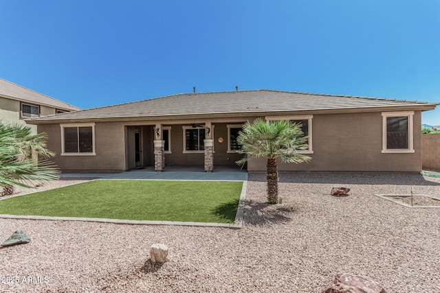 rear view of house featuring stucco siding, a tile roof, a yard, and a patio