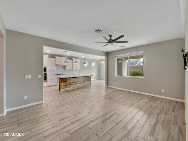 unfurnished living room with sink, ceiling fan with notable chandelier, and light hardwood / wood-style flooring