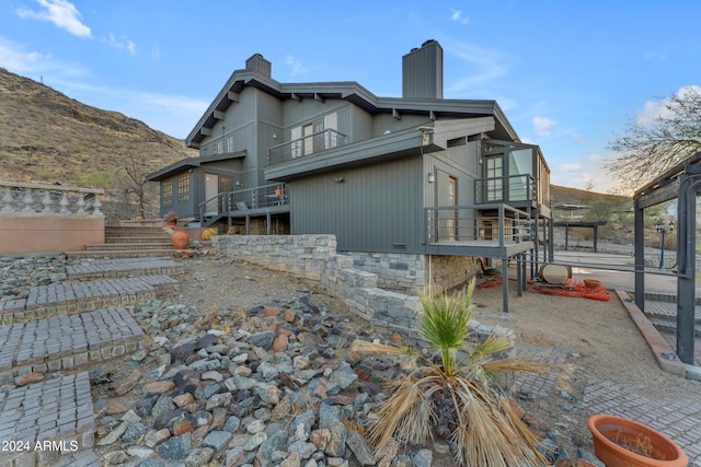 back of property with a balcony, a chimney, and stairway