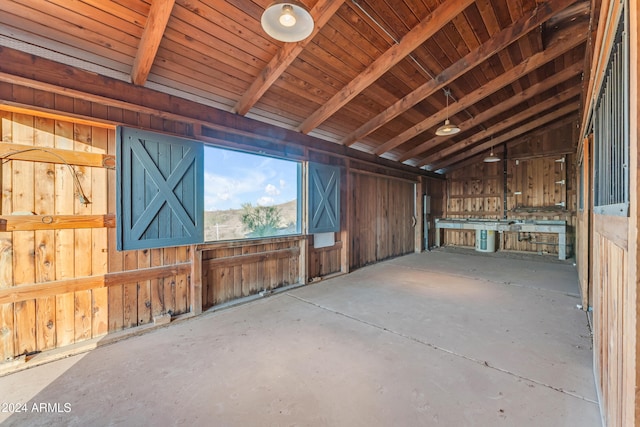 miscellaneous room featuring lofted ceiling with beams, wood walls, and concrete floors