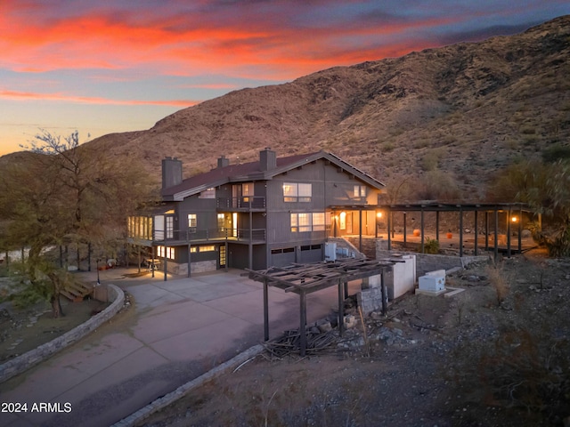 rear view of property with a chimney, concrete driveway, an attached garage, a mountain view, and a balcony