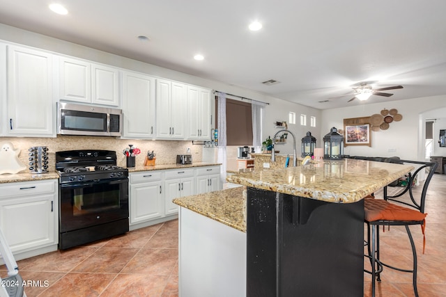 kitchen featuring stainless steel microwave, backsplash, black gas range, white cabinets, and a kitchen bar