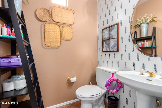 half bath with toilet, baseboards, a sink, and tile patterned floors