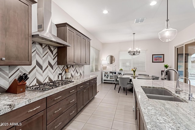 kitchen featuring sink, wall chimney exhaust hood, light stone countertops, decorative light fixtures, and stainless steel gas stovetop