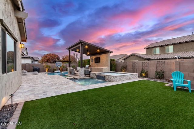 back house at dusk with a patio, a yard, ceiling fan, and a pool with hot tub