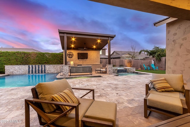 pool at dusk with pool water feature, an outdoor fireplace, an in ground hot tub, ceiling fan, and a patio