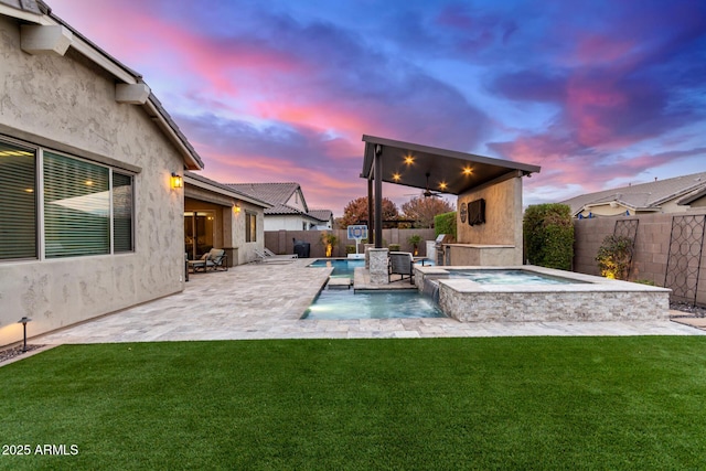 pool at dusk with pool water feature, a patio area, a lawn, an in ground hot tub, and ceiling fan