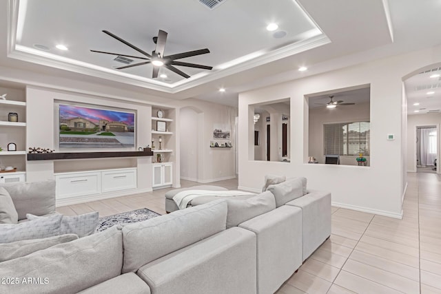 living room featuring light tile patterned flooring, ceiling fan, a tray ceiling, crown molding, and built in shelves