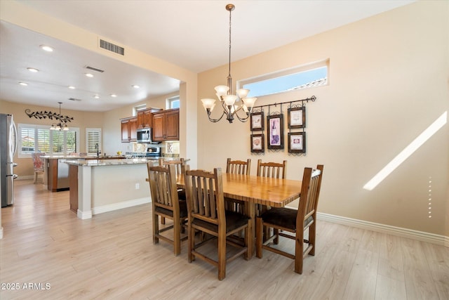 dining space with light wood finished floors, visible vents, a chandelier, and baseboards