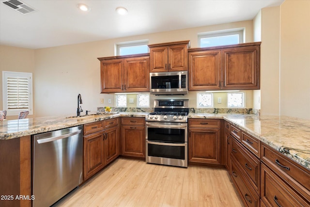 kitchen featuring brown cabinets, stainless steel appliances, visible vents, a sink, and a peninsula