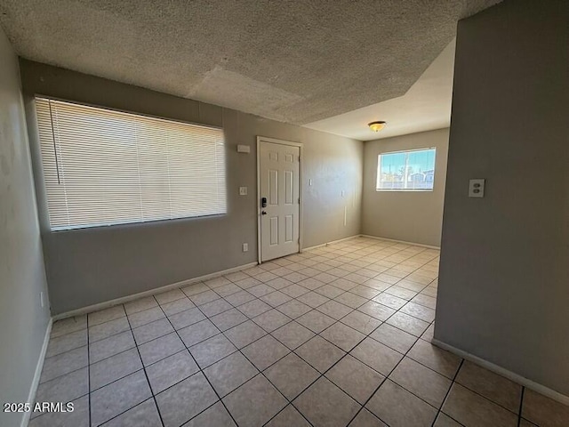 unfurnished room featuring light tile patterned floors, a textured ceiling, and baseboards