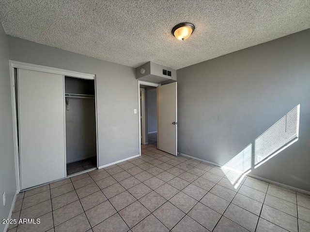 unfurnished bedroom featuring visible vents, baseboards, a closet, tile patterned floors, and a textured ceiling