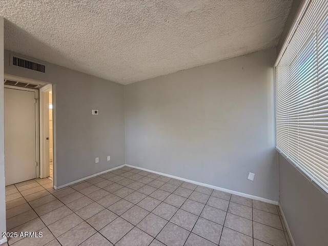 empty room featuring visible vents, baseboards, a textured ceiling, and light tile patterned flooring