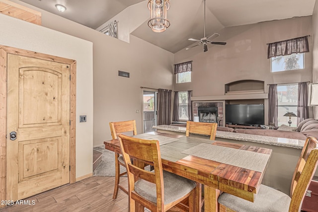 dining area with a fireplace, light wood-style floors, baseboards, ceiling fan, and high vaulted ceiling