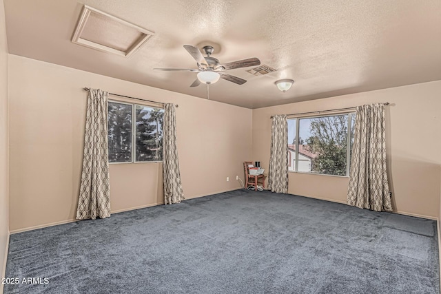 spare room featuring visible vents, carpet floors, attic access, ceiling fan, and a textured ceiling