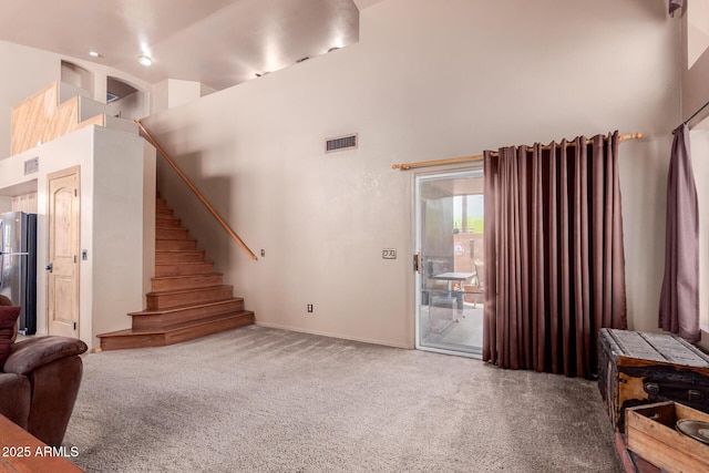 carpeted living area with stairway, baseboards, a high ceiling, and visible vents