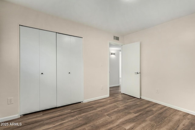 unfurnished bedroom with baseboards, visible vents, wood finished floors, and a closet
