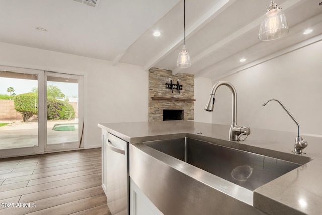 kitchen with stainless steel dishwasher, beam ceiling, a sink, light wood finished floors, and hanging light fixtures