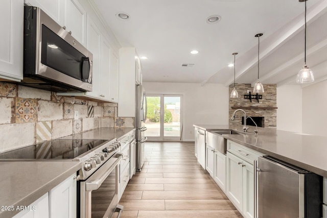 kitchen featuring a sink, light wood-style floors, stainless steel appliances, white cabinetry, and backsplash