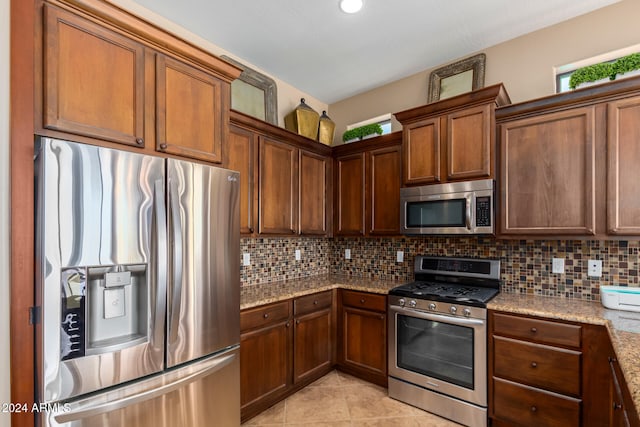 kitchen featuring decorative backsplash, stainless steel appliances, light stone counters, and light tile patterned flooring