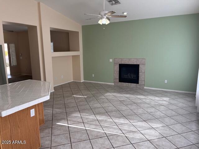 unfurnished living room with light tile patterned flooring, vaulted ceiling, ceiling fan, and a tiled fireplace