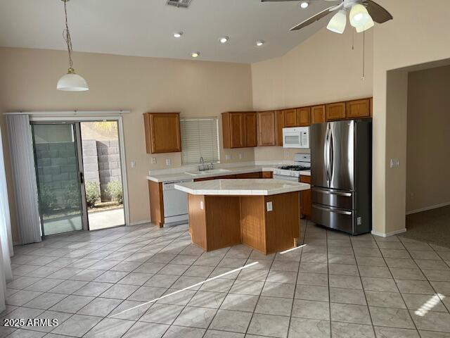 kitchen with pendant lighting, white appliances, sink, light tile patterned floors, and a kitchen island