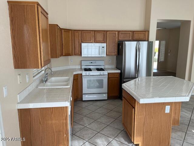 kitchen with tile counters, a center island, sink, white appliances, and light tile patterned flooring