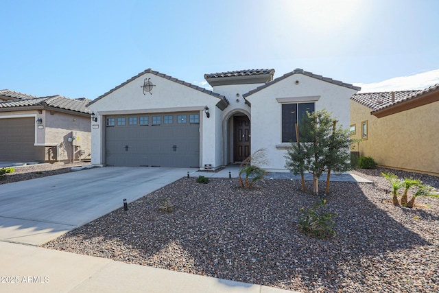 mediterranean / spanish-style home featuring a garage, a tile roof, concrete driveway, and stucco siding