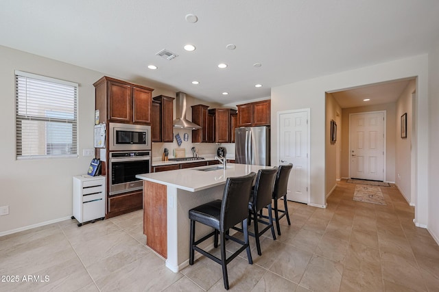 kitchen featuring visible vents, a breakfast bar, stainless steel appliances, light countertops, and wall chimney range hood