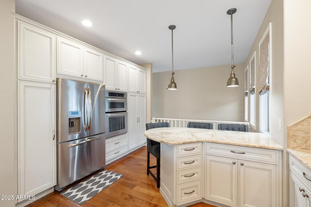 kitchen featuring light stone countertops, a peninsula, light wood-style flooring, appliances with stainless steel finishes, and a kitchen bar