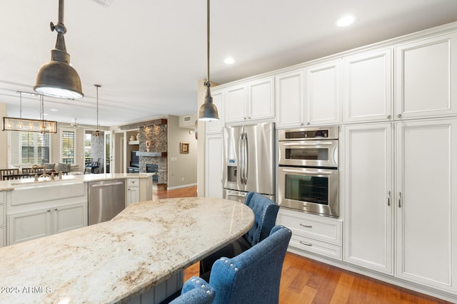 kitchen featuring light wood finished floors, a kitchen bar, a stone fireplace, stainless steel appliances, and a sink