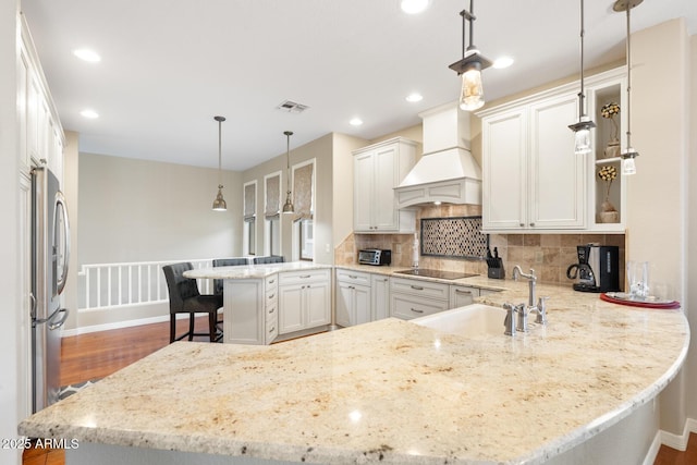 kitchen featuring a sink, tasteful backsplash, freestanding refrigerator, a peninsula, and custom exhaust hood