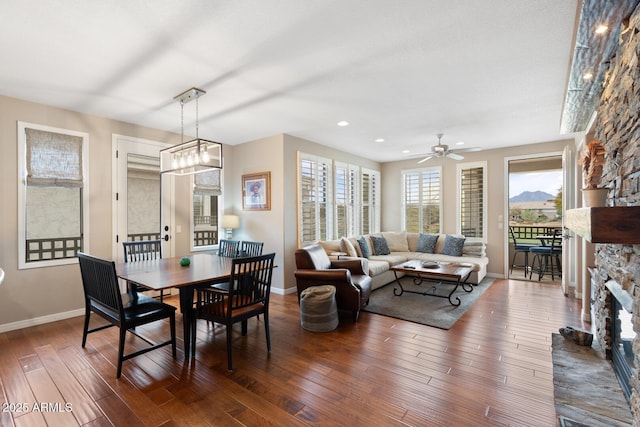 dining space featuring ceiling fan, baseboards, a stone fireplace, and wood finished floors